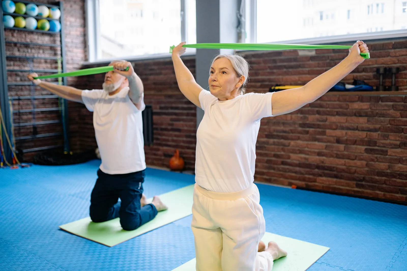Two active seniors doing resistance band exercises on mats in a bright studio. Photo by Yan Krukau on Pexels