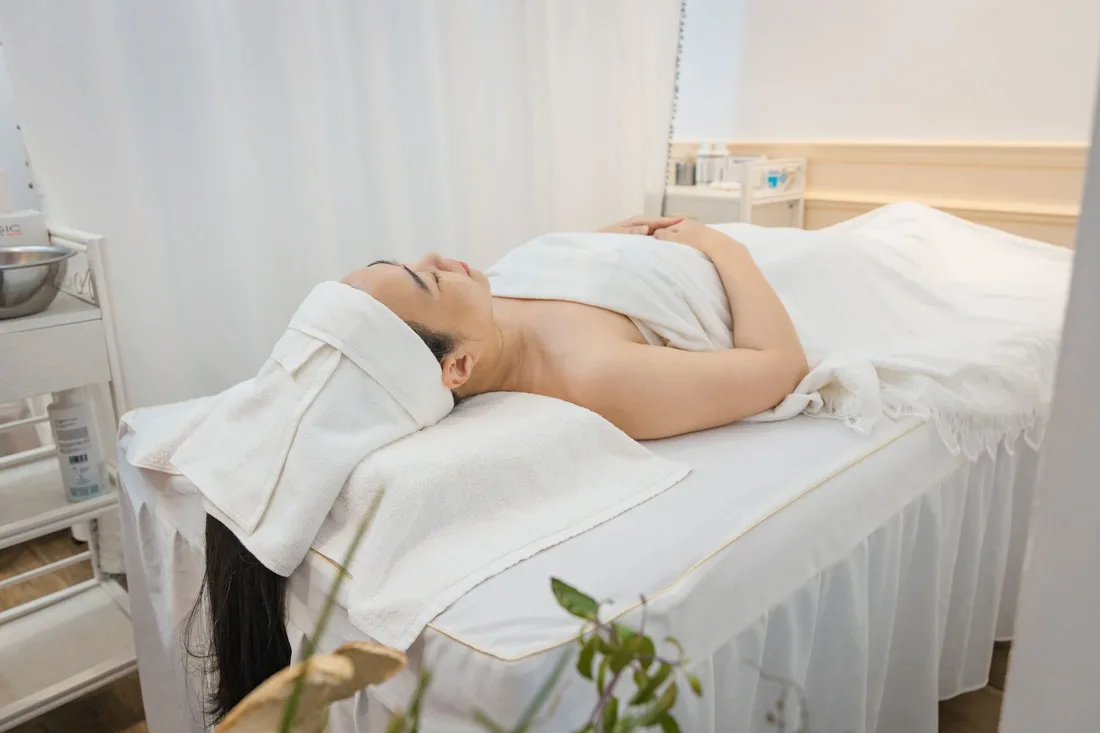 Woman relaxing on a white treatment bed in a bright aesthetic clinic room. Photo by HONG SON on Pexels
