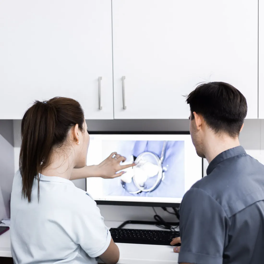 Two clinicians seen from behind at a white desk, one pointing at a monitor that shows a close-up of a tooth and a dental mirror. Photo by Bakytzhan Baurzhanov on Pexels