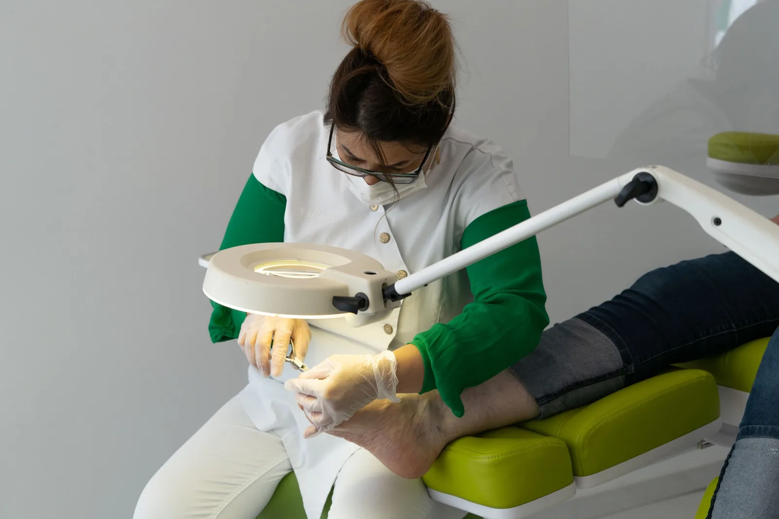 Podiatrist in a clinic chair treating a patient's foot under a magnifying lamp. Photo by Nico Becker on Pexels