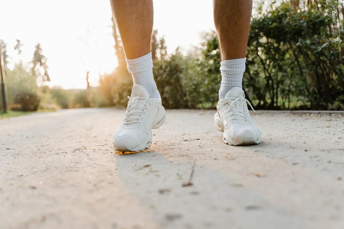 Person walking comfortably along a sunlit path in white sneakers. Photo by MART  PRODUCTION on Pexels