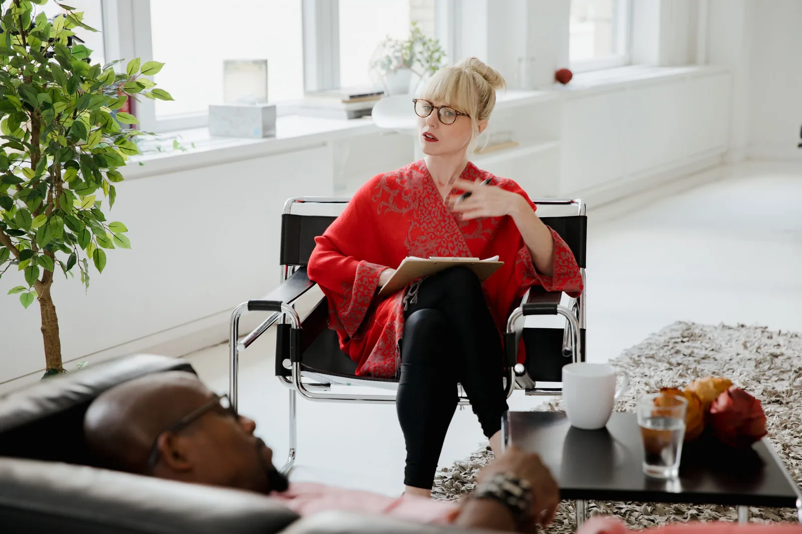 Therapist in a red top taking notes during a session in a bright, airy room. Photo by RDNE Stock project on Pexels
