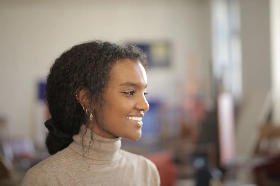 Smiling woman in a cream turtleneck looking relaxed and content indoors. Photo by Andrea Piacquadio on Pexels