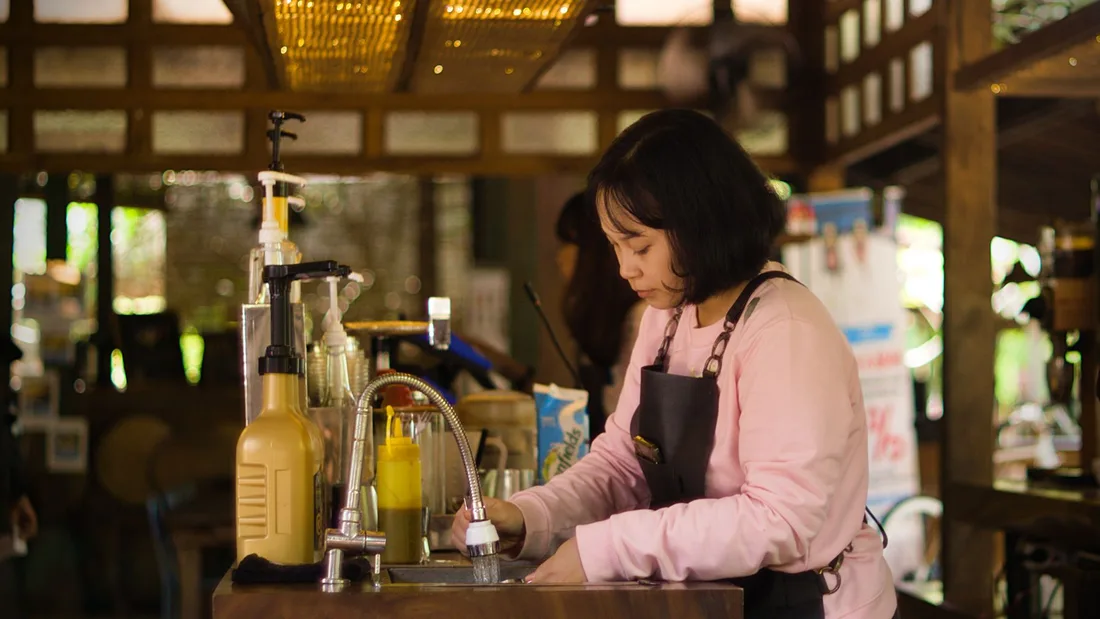 A female bartender washing dishes at a cozy, rustic bar with warm lighting. Photo by Yudinda Gilang Pramudya on Pexels