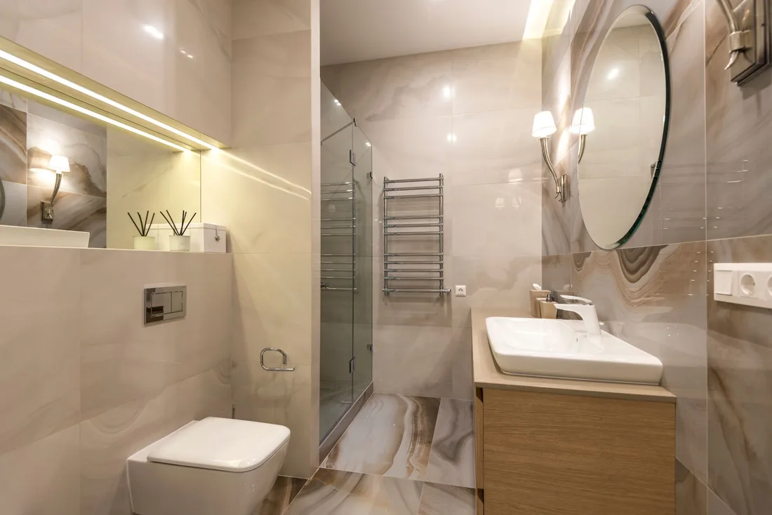Finished modern bathroom with a wood vanity, round mirror and glass shower. Photo by Max Vakhtbovych on Pexels