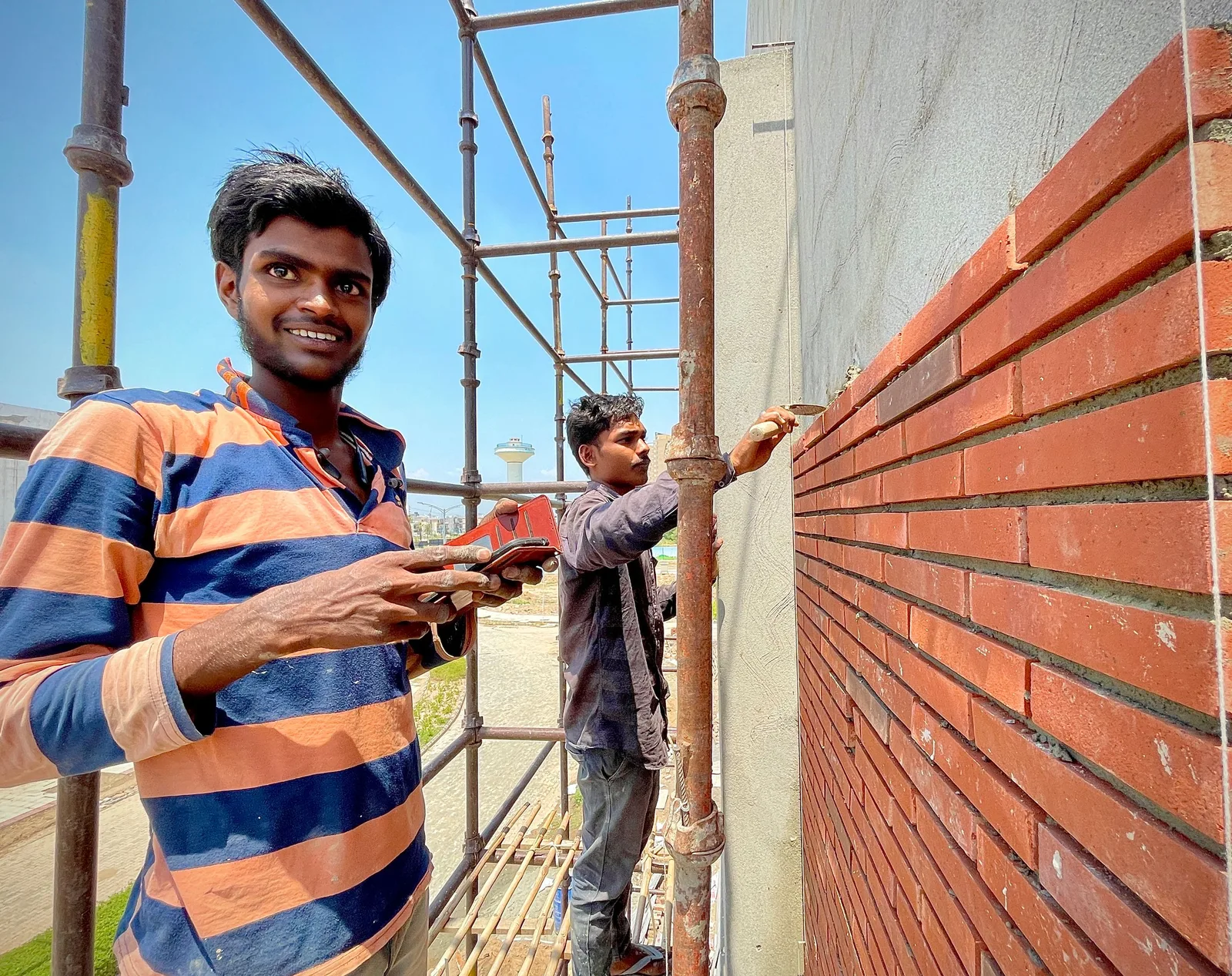 Two construction workers laying red bricks on scaffolding outside a building. Photo by Nishant Aneja on Pexels