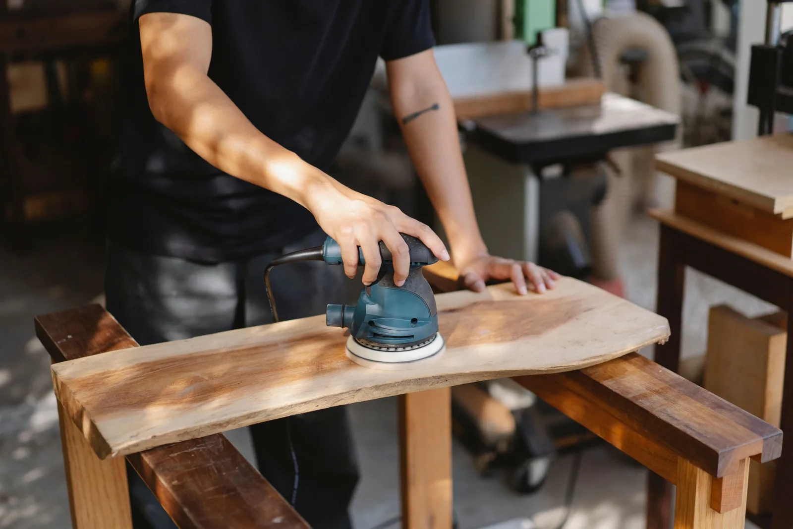 Carpenter sanding a live-edge wooden tabletop with an electric sander in a workshop. Photo by Ono  Kosuki on Pexels