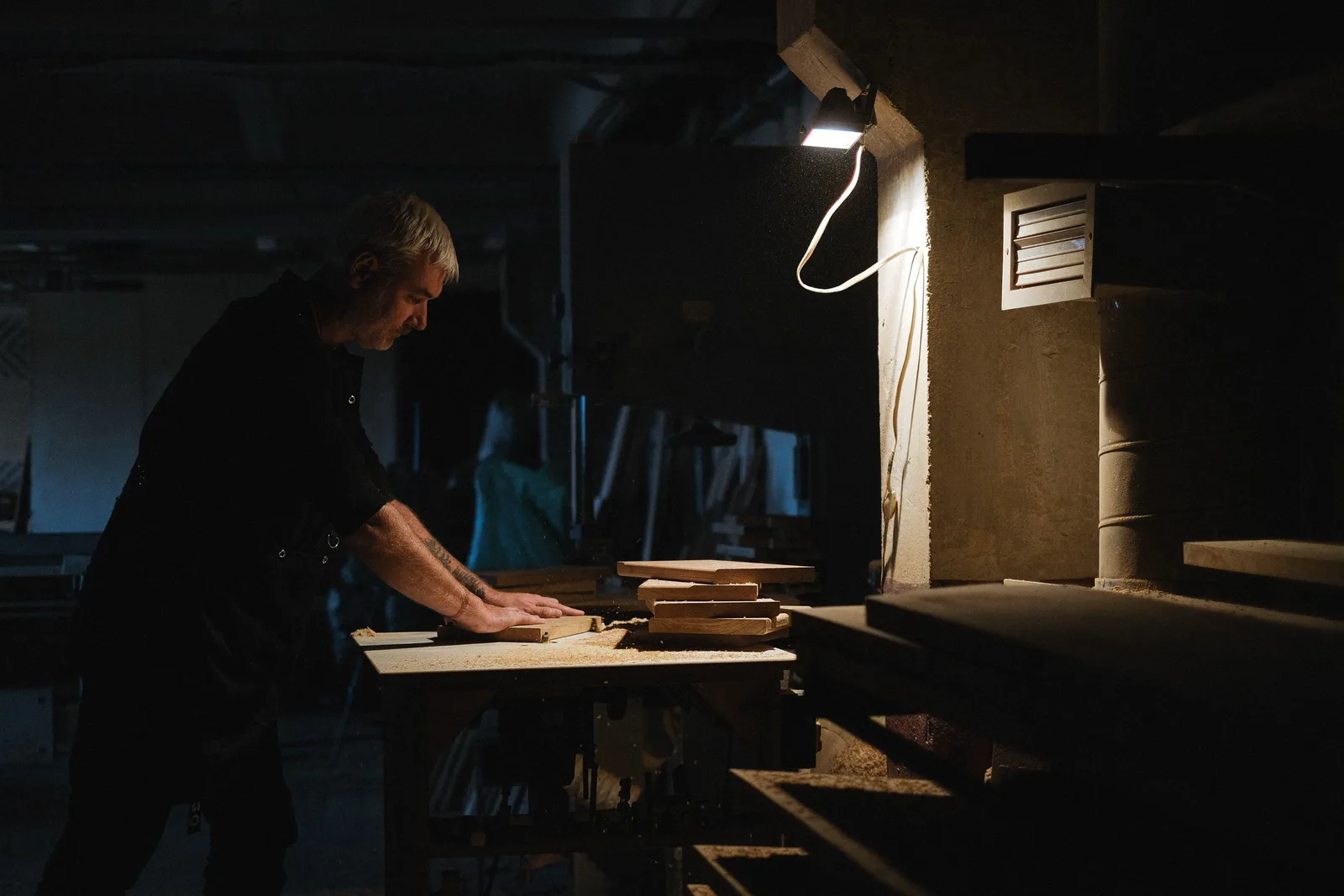 Side view of skilled male master processing wooden board while working at workbench in dark workshop with glowing lamp. Photo by Anna Shvets on Pexels