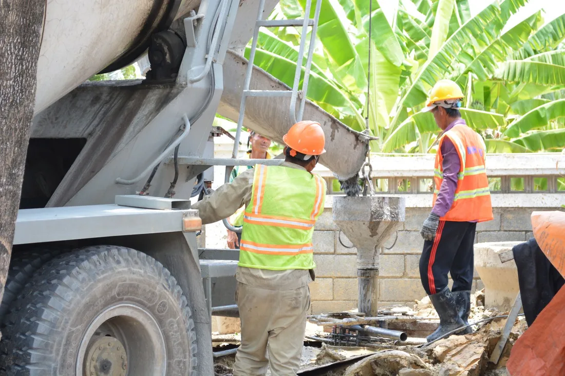 Construction site with workers pouring concrete from a truck chute outdoors. Photo by SÀI GÒN CÔNG TY CP SẢN XUẤT - THƯƠNG MẠI on Pexels
