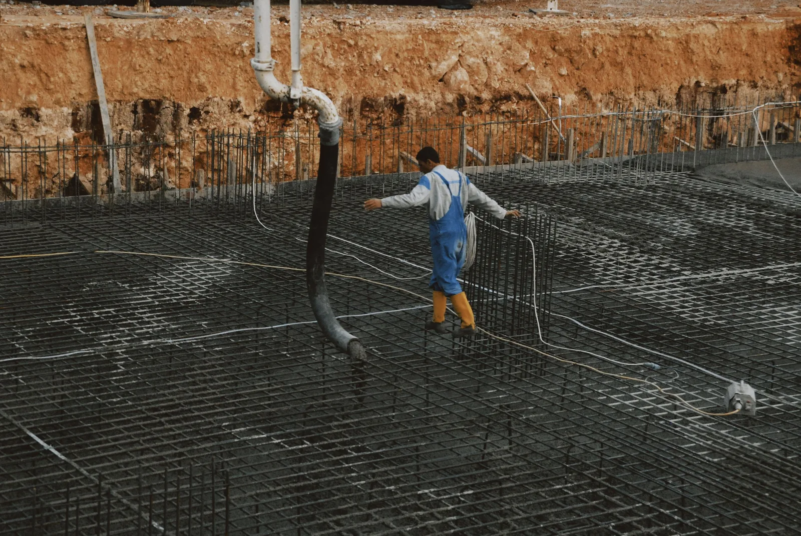 A construction worker in yellow boots walks on rebar grid at a building site. Photo by Mehmet Turgut  Kirkgoz on Pexels