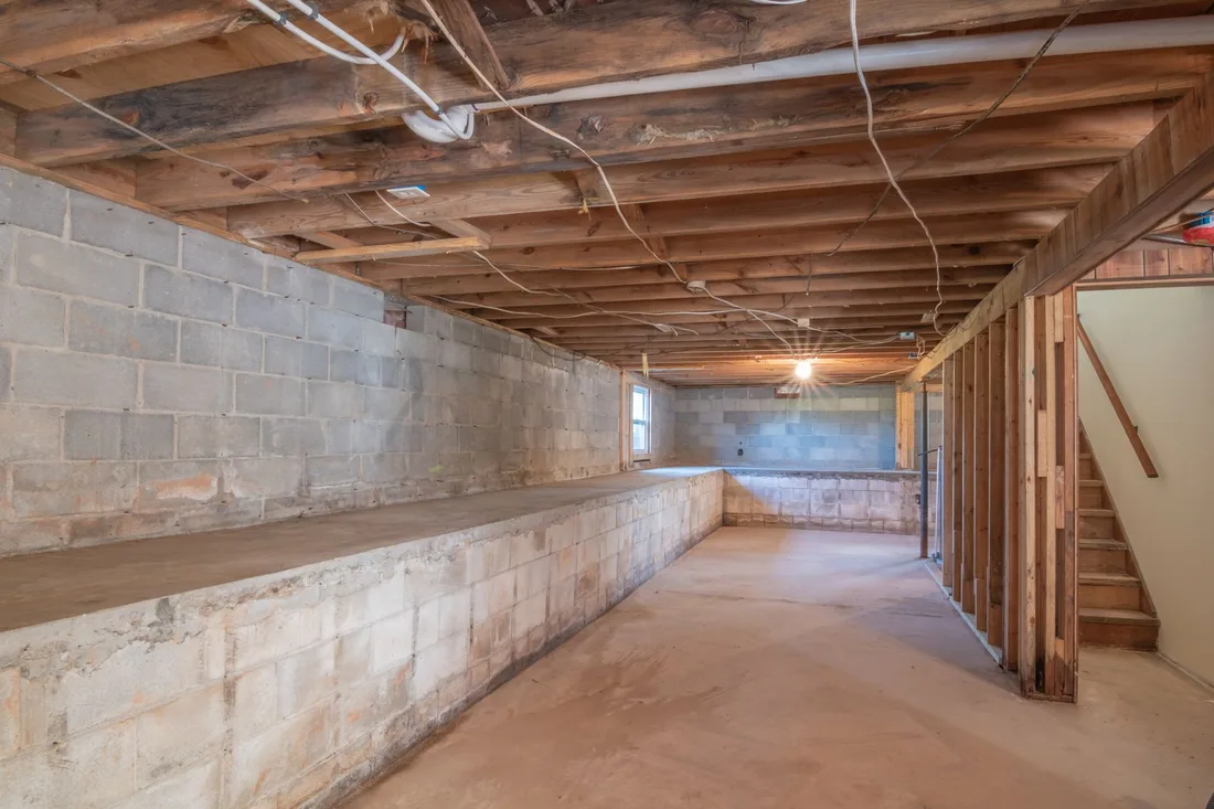 Empty basement with exposed wooden beams, concrete walls and stairs. Photo by Curtis Adams on Pexels