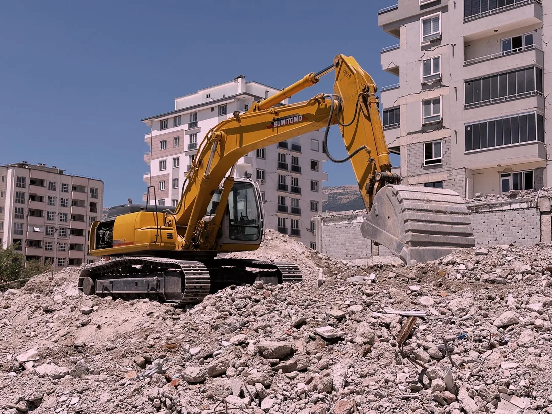 Yellow excavator working on urban construction site amidst rubble and buildings in Kahramanmaraş, Türkiye. Photo by Niyazi Gökdoğan on Pexels