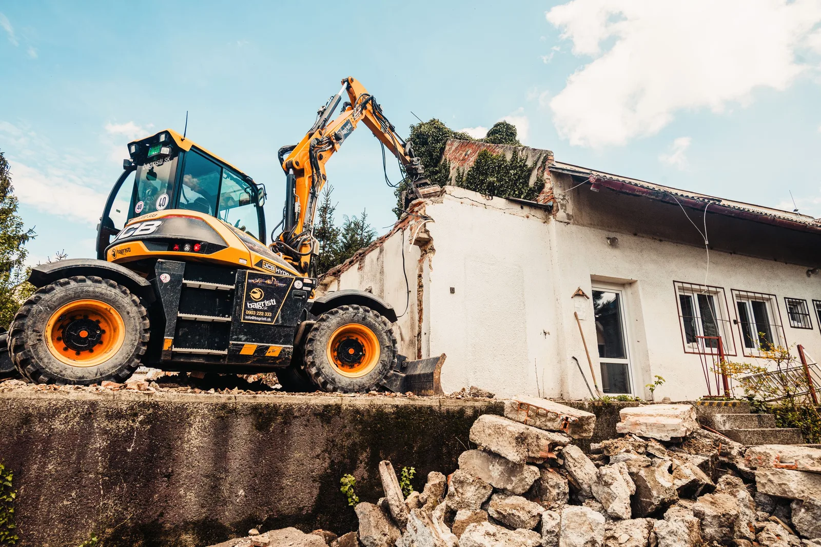 Compact excavator with grapple demolishing a small building with rubble in the foreground. Photo by Helena Jankovičová Kováčová on Pexels