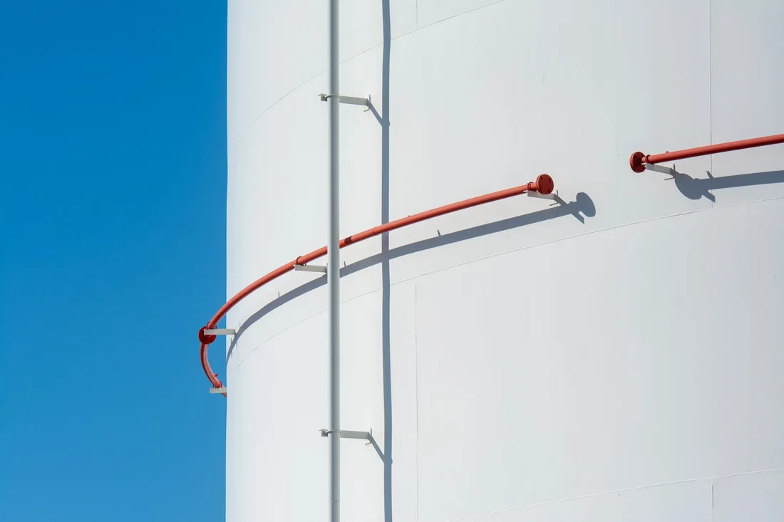 Close-up of a white industrial tank with a curved red duct against a blue sky. Photo by Jan van der Wolf on Pexels