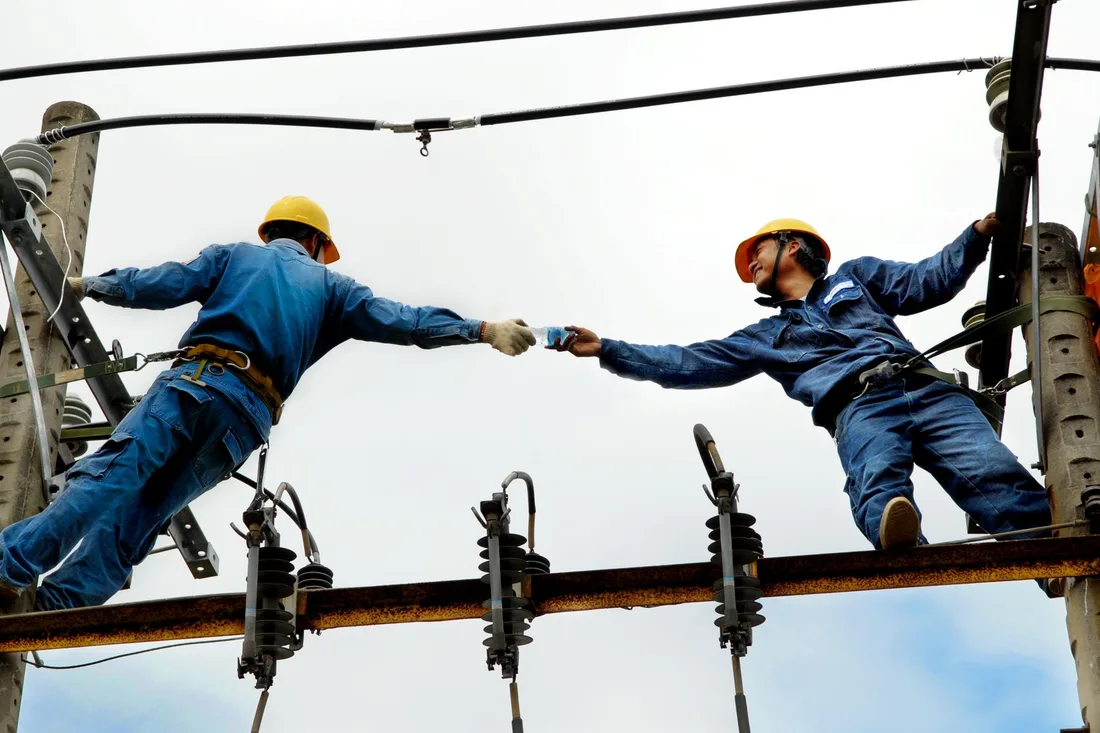 Two electrical workers in blue uniforms collaborating on power lines during daytime. Photo by Tuấn Nguyễn Văn on Pexels