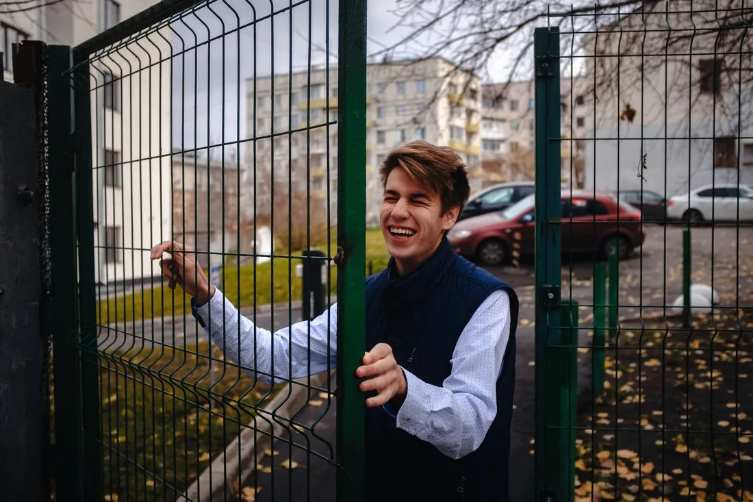 Happy young man in a blue vest entering through an open metal gate on a fall day in the city. Photo by Vova Kras on Pexels