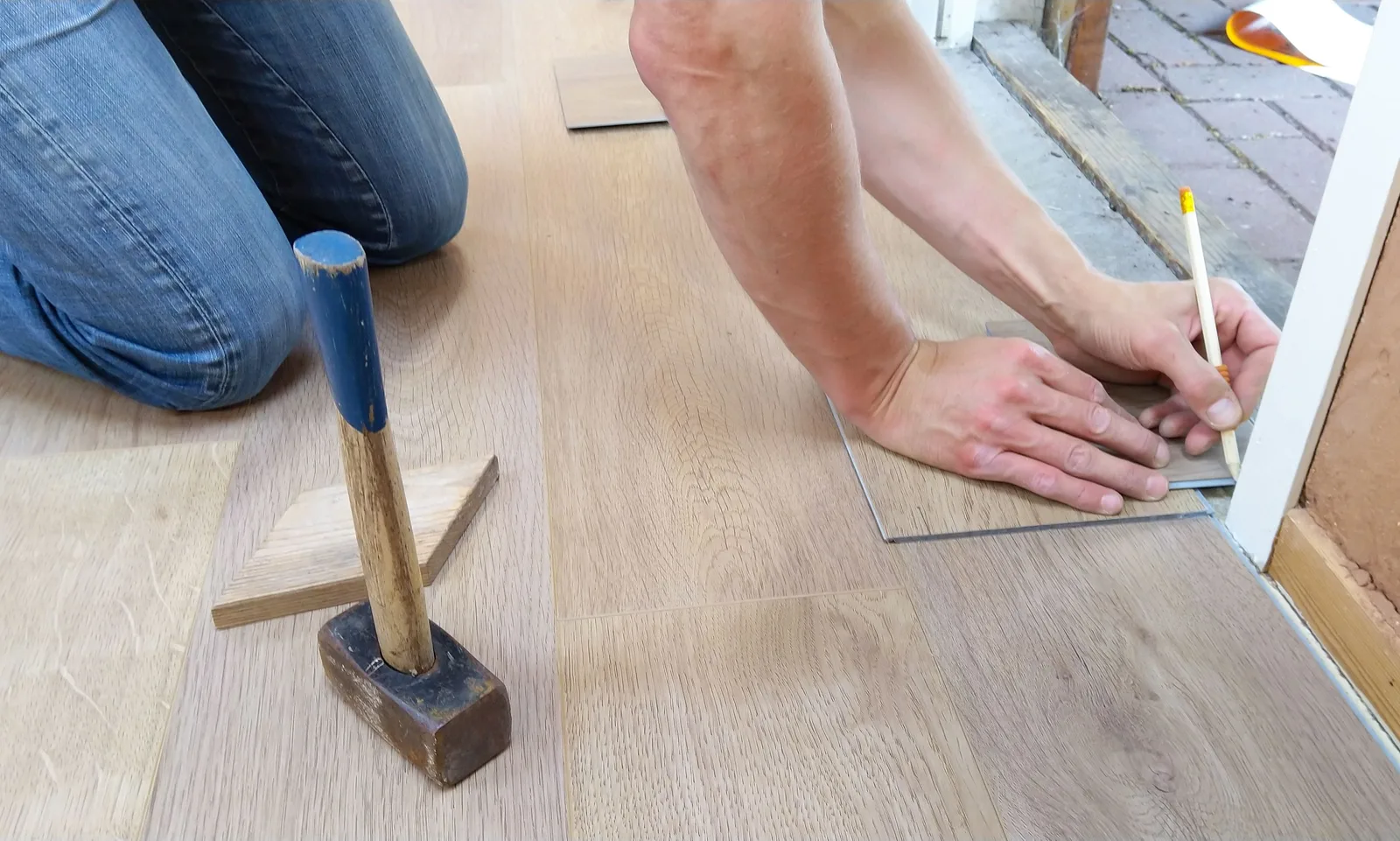 A craftsman carefully measures and marks wooden floor panels for precise installation. Photo by ClickerHappy on Pexels