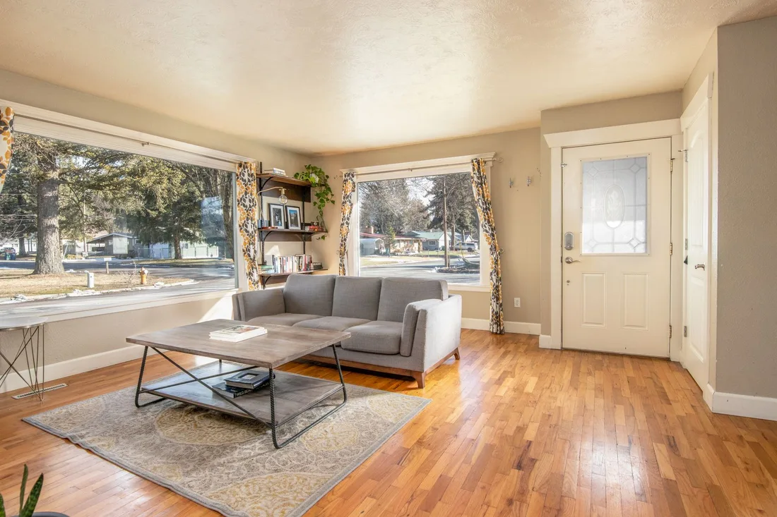 Furnished living room with a finished hardwood floor, sofa and large window. Photo by Clay Elliot on Pexels