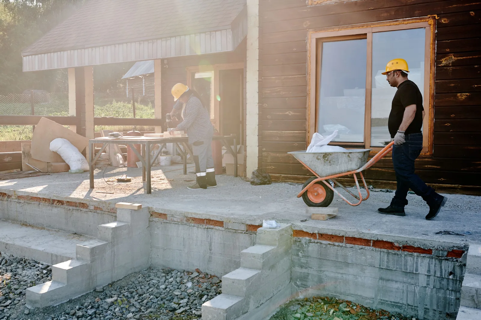 Construction workers with a wheelbarrow at a freshly poured concrete foundation and steps. Photo by Mikael Blomkvist on Pexels