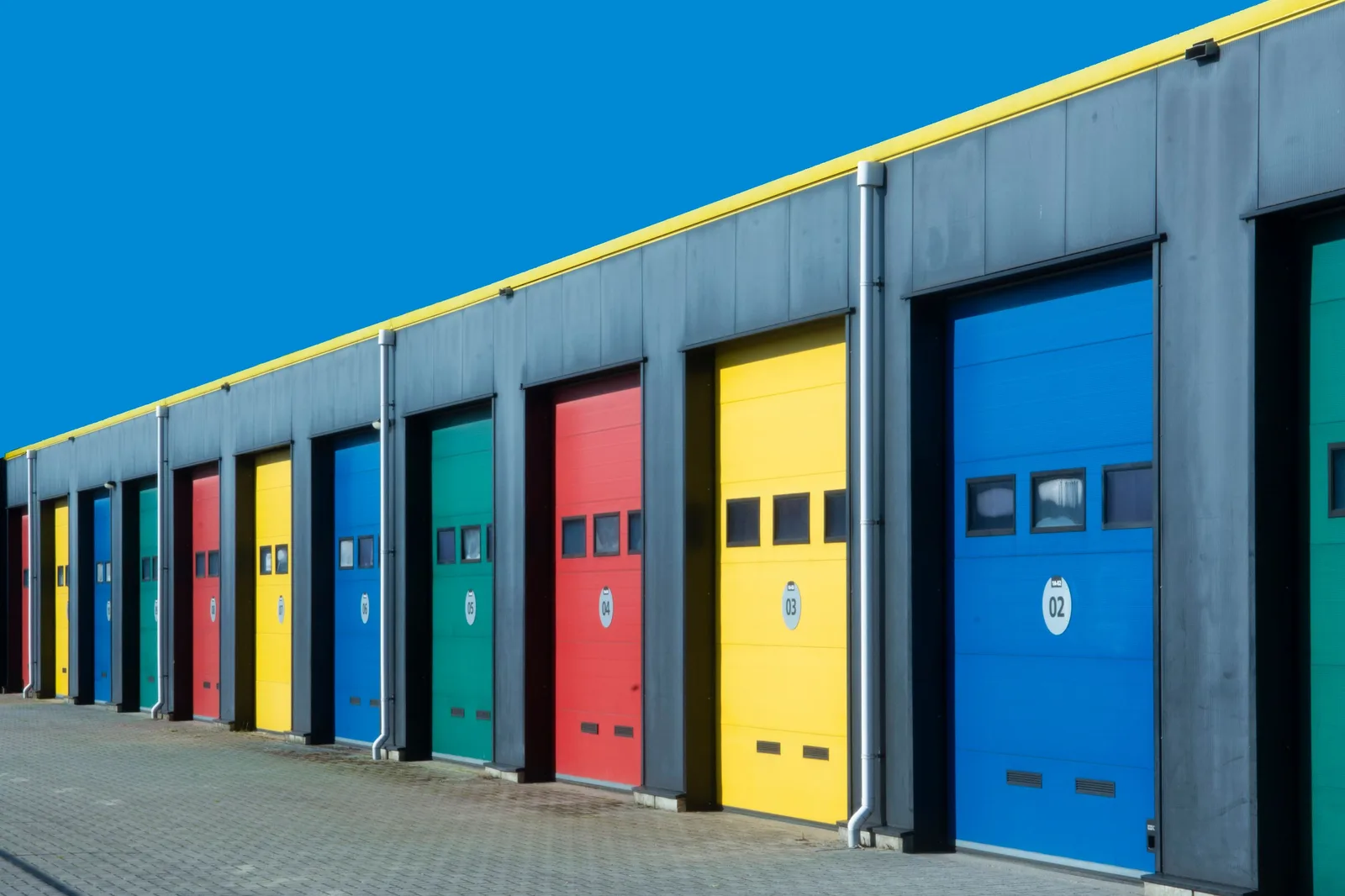 Vibrant row of industrial garage doors in blue, red, yellow, and green, perfect for commercial use. Photo by Jan van der Wolf on Pexels