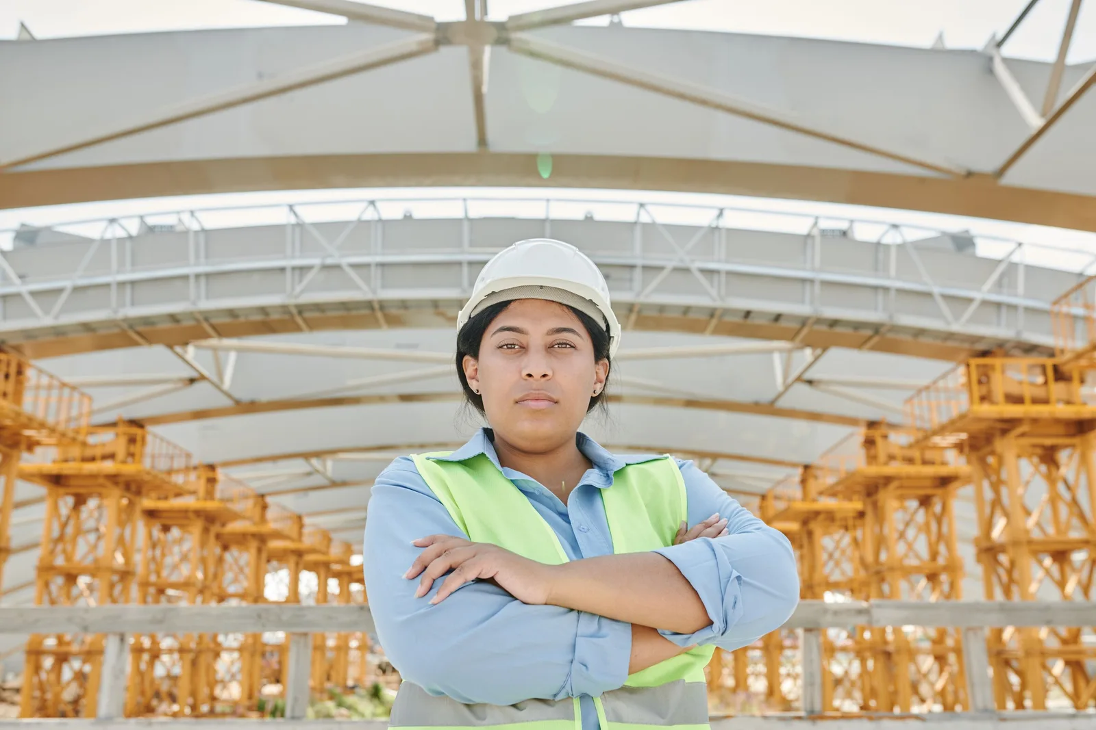 Female contractor in hard hat and safety vest standing with arms crossed on a building site. Photo by Mikael Blomkvist on Pexels