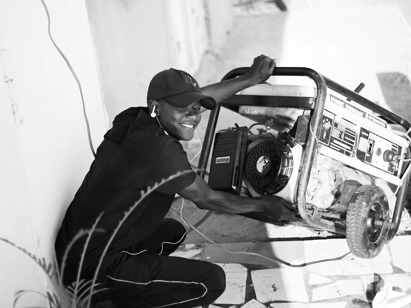 A cheerful young man wearing a cap and earphones operating a portable generator outside. Photo by Abdulkadir muhammad sani on Pexels