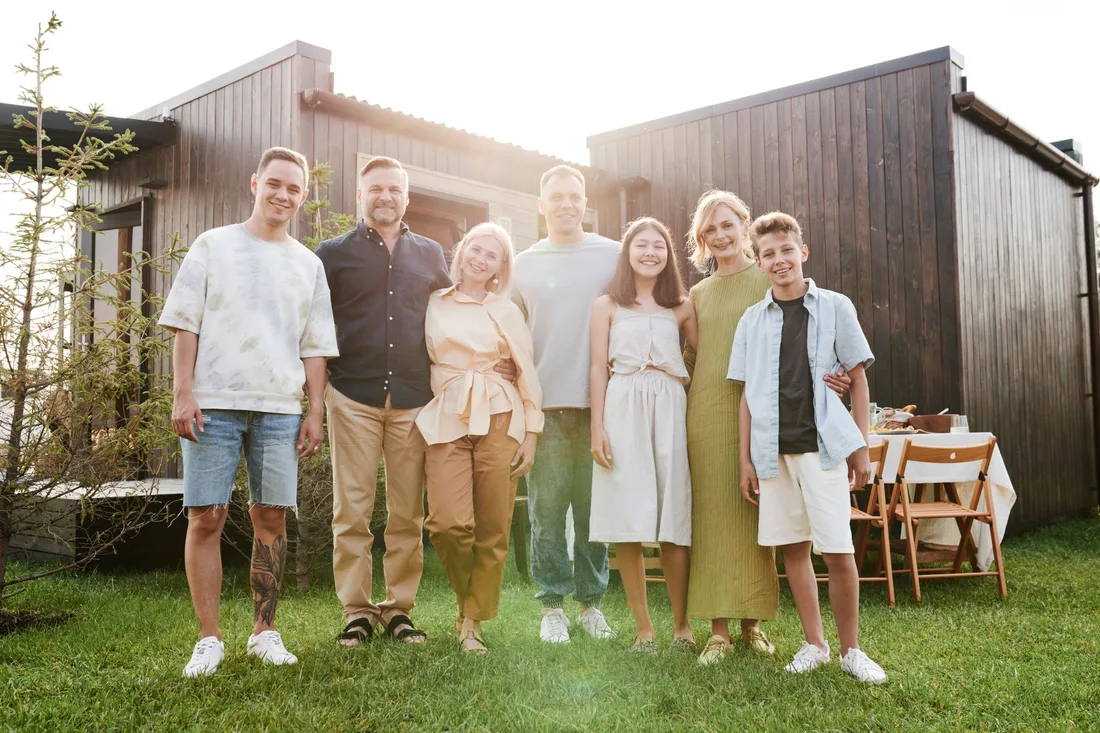Family of six standing together outside a modern house with a wooden dining table. Photo by Julia M Cameron on Pexels