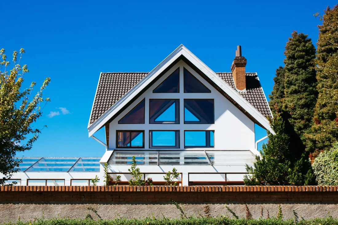 Modern white house with large glazed windows under a clear blue sky. Photo by Athena Sandrini on Pexels