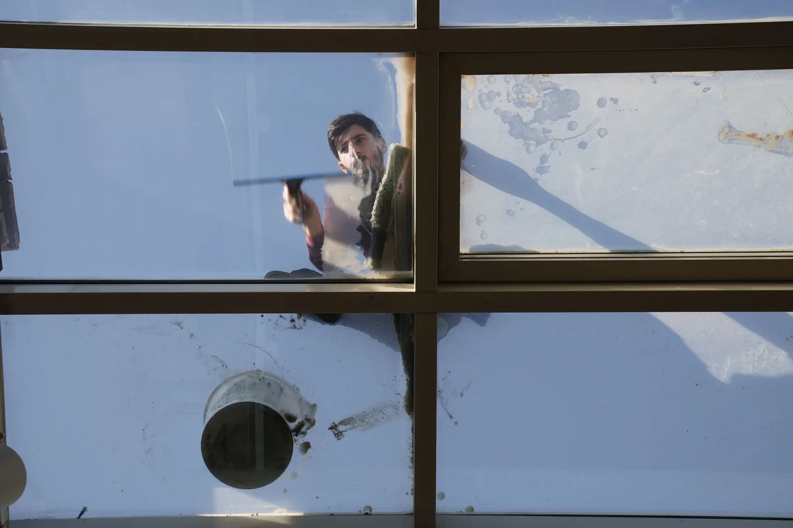 A male window cleaner washing the exterior glass roof from above with a tool during daylight. Photo by Tahir Xəlfəquliyev on Pexels
