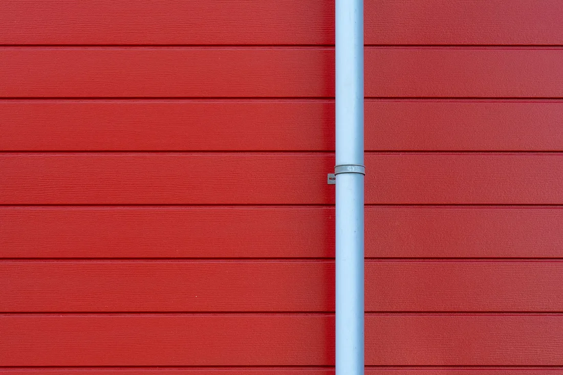 A minimalist photo of a red wall with a white rain gutter, showing clean lines and vibrant color contrast. Photo by Jan van der Wolf on Pexels