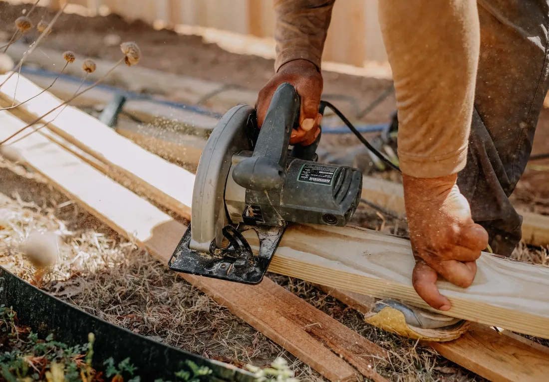 Carpenter operating a circular saw on wooden planks outside, showcasing woodworking skills. Photo by Daniel Agundiz on Pexels
