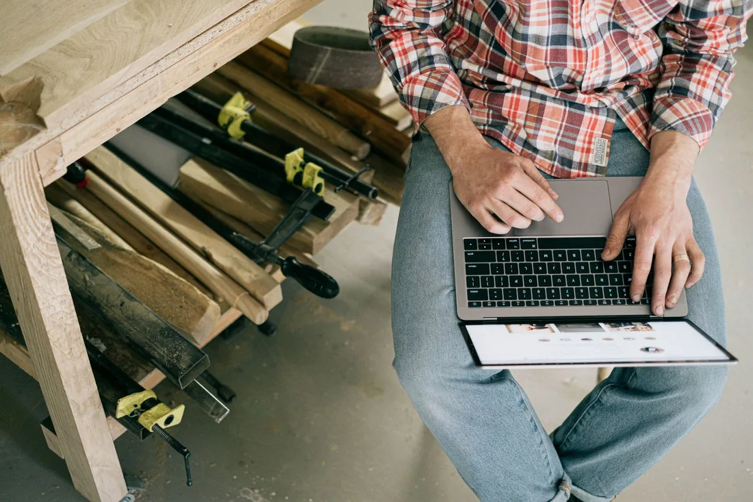 A craftsman using a laptop in a woodworking workshop, focusing on online research or design. Photo by Ivan S on Pexels
