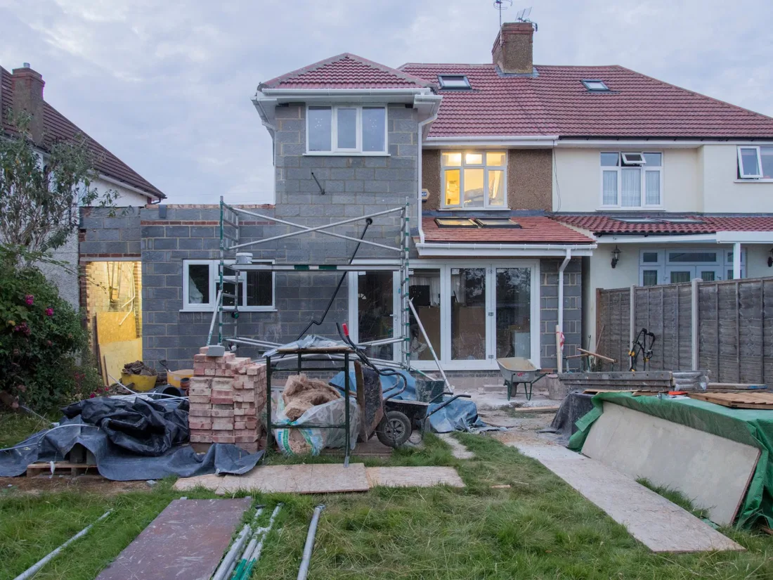 A suburban house undergoing major renovations with scaffolding and building materials. Photo by Brett Jordan on Pexels