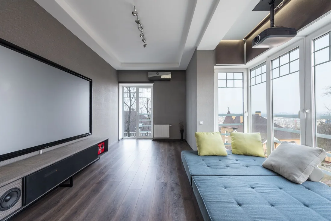 Spacious media room with projector screen, blue daybed and large windows. Photo by Max Vakhtbovych on Pexels