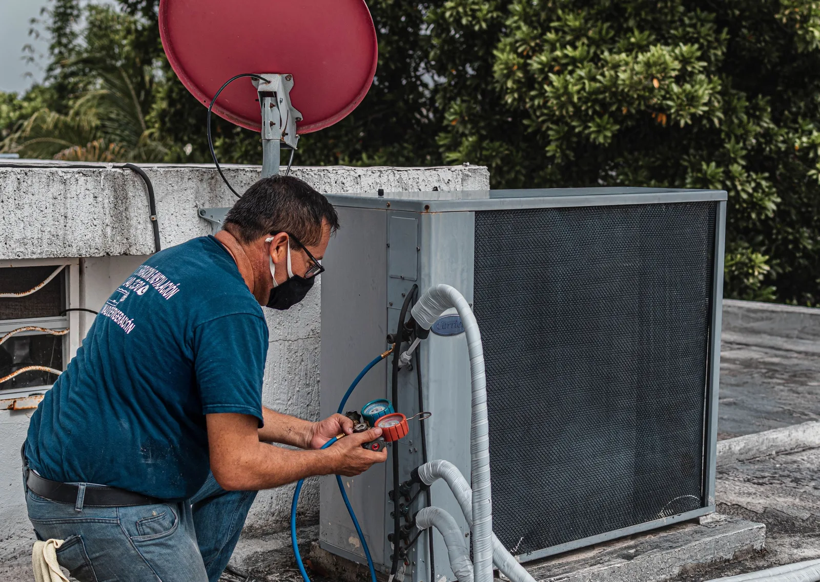 Technician repairing an air conditioner unit outdoors, wearing a facemask and using a manifold gauge. Photo by José Andrés  Pacheco Cortes on Pexels