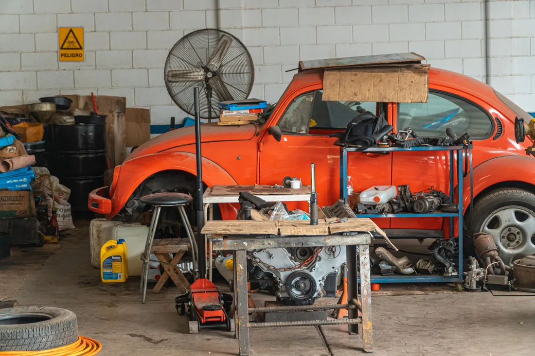 Cluttered garage workshop with an orange vintage car, tools and stored items. Photo by Jose Ricardo Barraza Morachis on Pexels