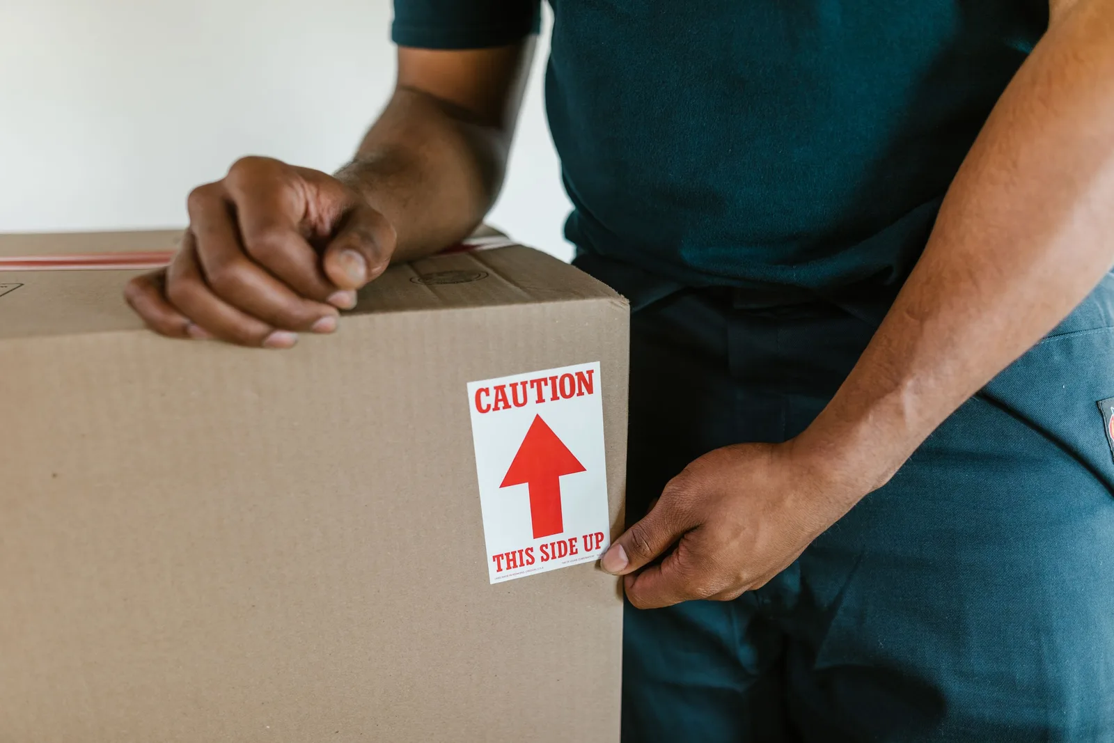 A person handling a moving box with a 'caution this side up' label indoors. Photo by RDNE Stock project on Pexels