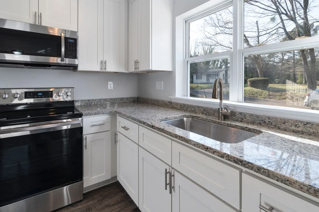 Finished modern kitchen with white cabinets, granite counters and a large window. Photo by Curtis Adams on Pexels