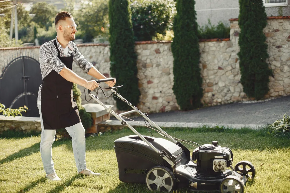 A man using a lawn mower to trim grass in a sunny outdoor garden. Photo by Gustavo Fring on Pexels