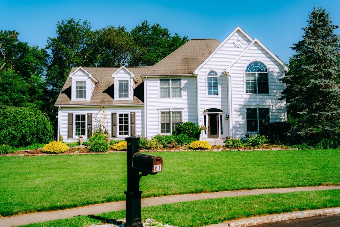 White suburban house with landscaped garden and a neatly cut green lawn. Photo by Diogo Miranda on Pexels