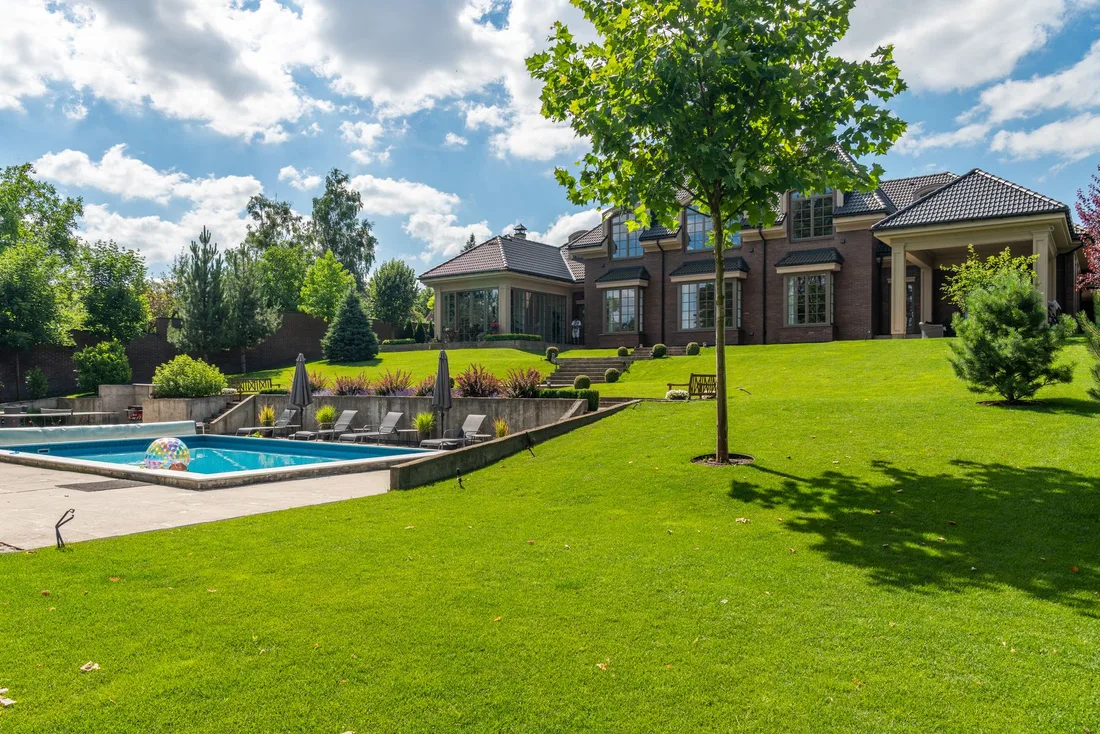 Large manicured green lawn with trees and a house in the background. Photo by Max Vakhtbovych on Pexels