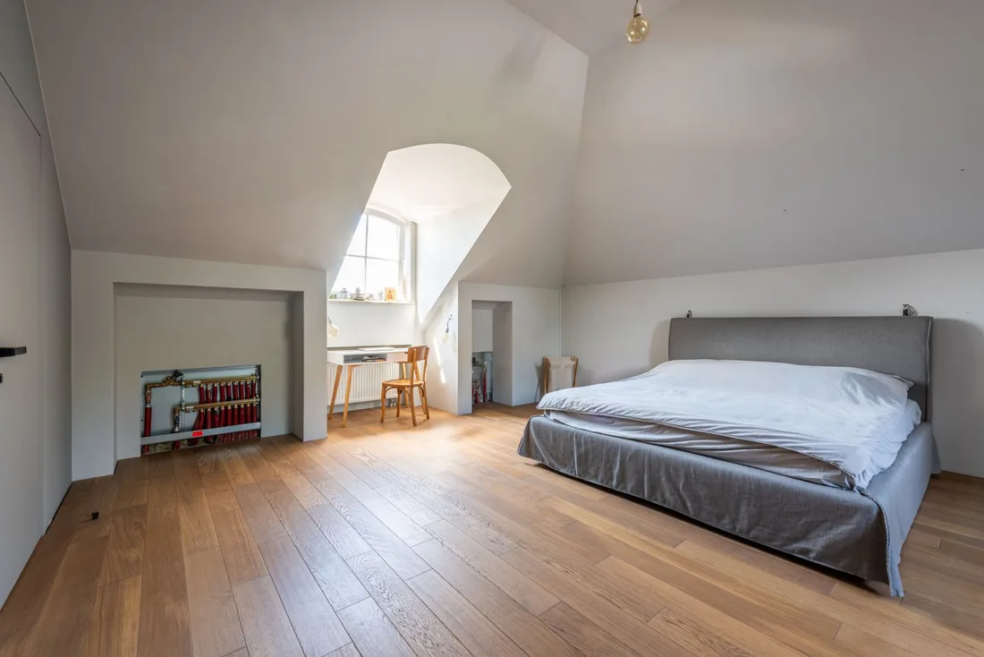 Bright attic bedroom with sloped white ceiling, window and gray bed in the UK. Photo by Max Vakhtbovych on Pexels