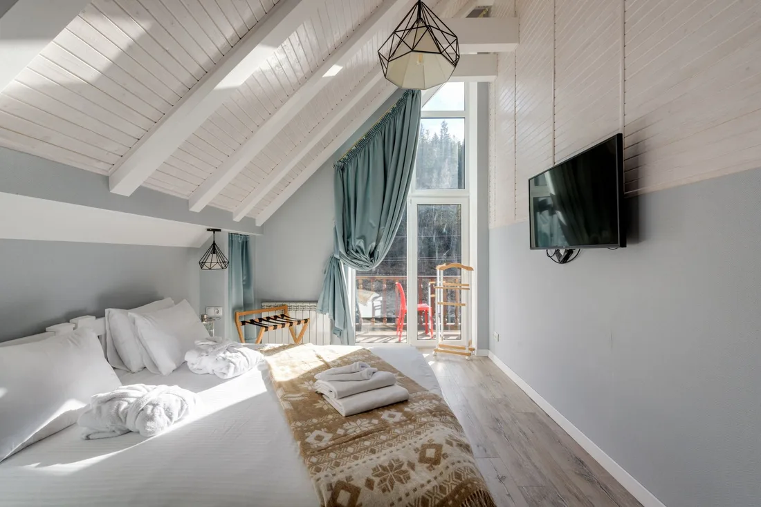 Finished loft bedroom with sloped wood ceiling, green curtains and wall television in the UK. Photo by Max Vakhtbovych on Pexels