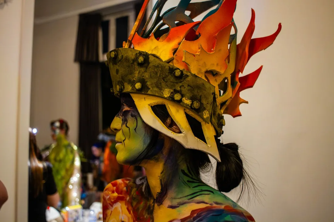 Vibrant portrait of a person with artistic body paint and an elaborate flame-inspired helmet indoors. Photo by Cord Allman on Pexels