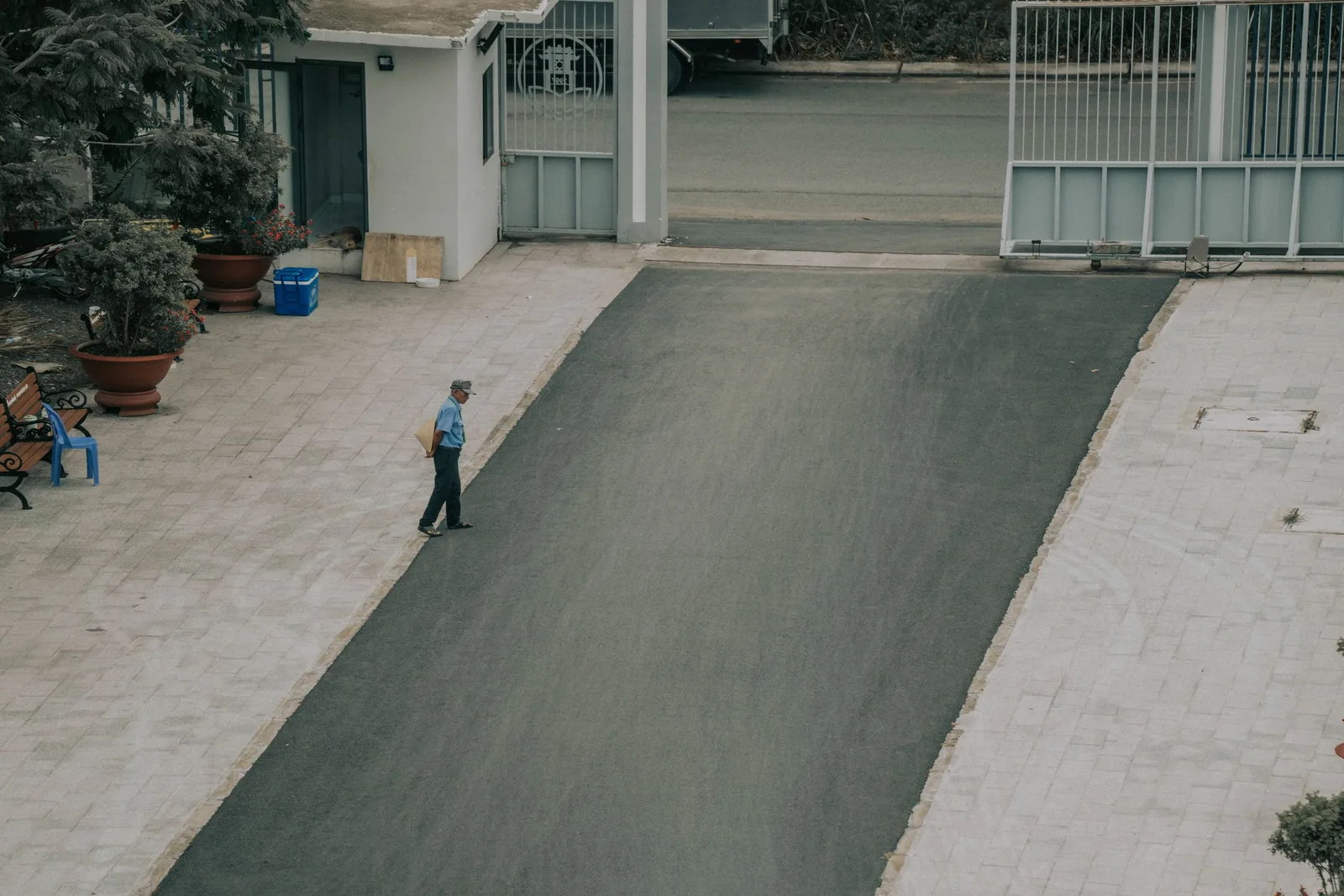 Aerial view of a man walking on a paved driveway lined with potted plants and a gate. Photo by Nguyễn Hoàng Văn on Pexels