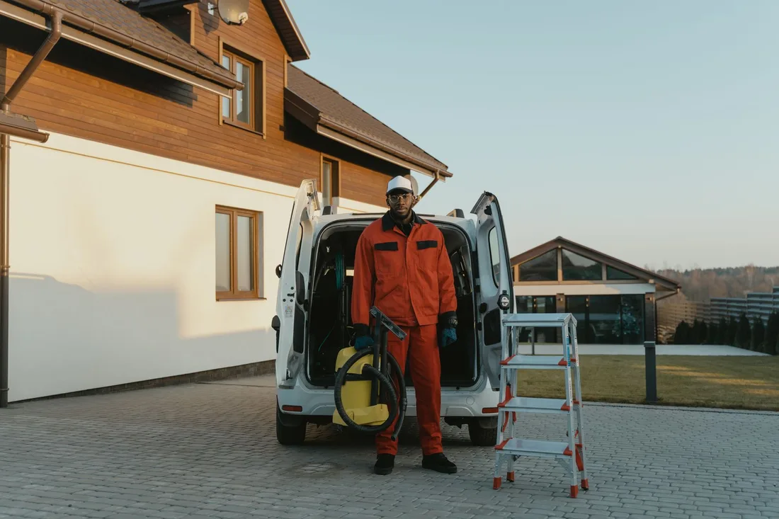 A male worker in red coveralls with a vacuum cleaner beside a van on a sunny day. Photo by Tima Miroshnichenko on Pexels