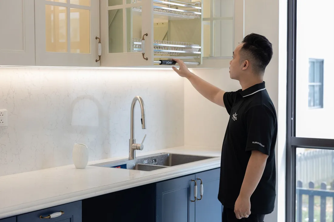 Pest inspector in a dark uniform checking kitchen cabinets above the sink in a bright kitchen. Photo by HONG SON on Pexels