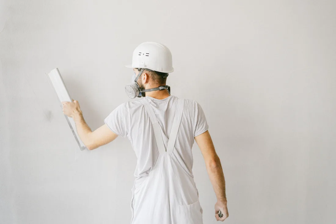 Back view of a construction worker in safety gear plastering a white wall. Photo by AI25.Studio  Studio on Pexels