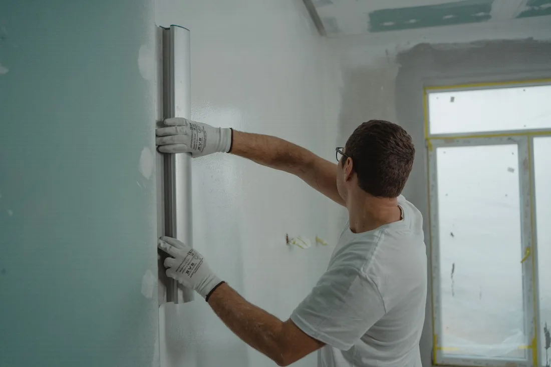 Plasterer smoothing a wall with a long float in a room with a window. Photo by Tima Miroshnichenko on Pexels
