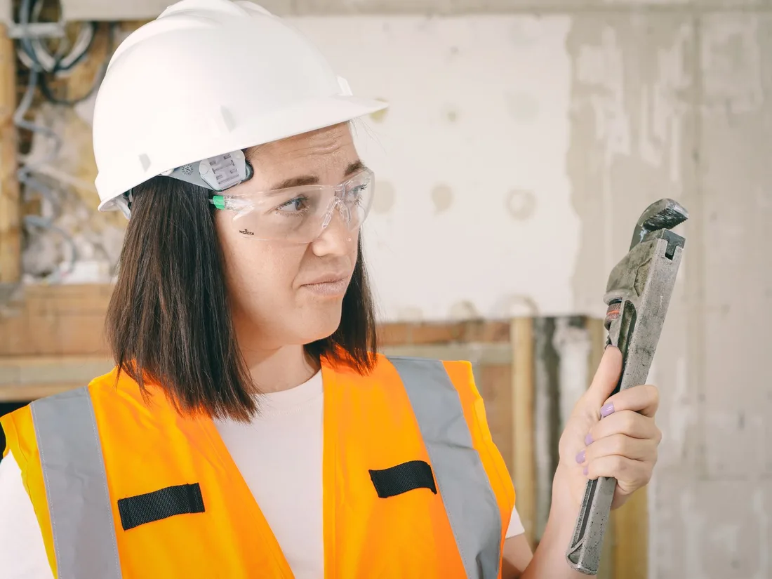 Caucasian woman in PPE holding a plumber's wrench indoors, focused on maintenance. Photo by Kindel Media on Pexels